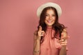 A dark-haired girl in a pink dress openly smiling looks at the camera and points her fingers forward on a pink Royalty Free Stock Photo