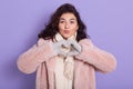 Dark haired girl stands isolated over lilac background, shows heart gesture with her fingers, lady showing love gesture, wears