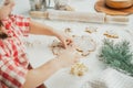 Dark-haired girl 3 years old in red Christmas cap and checkered shirt cuts out gingerbread cookies from rolled dough Royalty Free Stock Photo