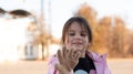 Dark-haired little girl in a jacket with a hood smiling stretches out her hand in a glove standing on the autumn street
