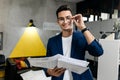 Dark-haired stylish architect in glasses dressed in blue checkered jacket and jeans works with blueprints in the modern Royalty Free Stock Photo