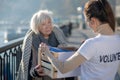 Dark-haired volunteer giving box with clothing to poor homeless woman