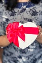 Dark-haired woman holding a gift box in a heart shape with red bow. Concept of  New Year, Christmas and Valentine`s Day Royalty Free Stock Photo