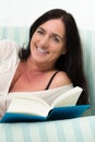Dark haired woman lying on couch and reading a book
