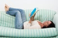 Dark haired woman lying on couch and reading a book Royalty Free Stock Photo