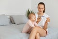 Dark haired woman wearing white t shirt and shorts sitting on bed with her baby daughter and holding pregnancy test with negative Royalty Free Stock Photo