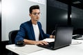 Dark-haired young architect dressed in a blue jacket works on the laptop in the office Royalty Free Stock Photo