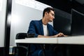 Dark-haired young architect dressed in a blue jacket works on the laptop in the office Royalty Free Stock Photo