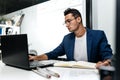 Dark-haired young architect dressed in a blue jacket works on the laptop in the office Royalty Free Stock Photo