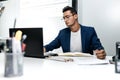 Dark-haired young architect in glasses and in a blue jacket is working with documents on the desk in the office Royalty Free Stock Photo