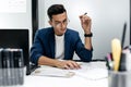 Dark-haired young architect in glasses and in a blue jacket is working with documents on the desk in the office Royalty Free Stock Photo