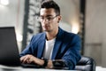 Dark-haired young architect in glasses dressed in blue checkered jacket works on the laptop in the office Royalty Free Stock Photo