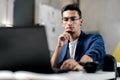 Dark-haired young architect in glasses dressed in blue checkered jacket works on the laptop in the office Royalty Free Stock Photo