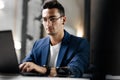 Dark-haired young architect in glasses dressed in blue checkered jacket works on the laptop in the office Royalty Free Stock Photo