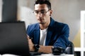 Dark-haired young architect in glasses dressed in blue checkered jacket works on the laptop in the office Royalty Free Stock Photo