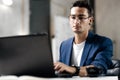 Dark-haired young architect in glasses dressed in blue checkered jacket works on the laptop in the office Royalty Free Stock Photo