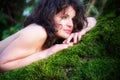 Dark-haired young woman is lying happily contentedly in an old willow tree on the green moss with bare shoulders and smile Royalty Free Stock Photo