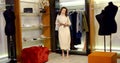 A dark-haired young slender woman is in a large women`s wardrobe fitting room with mannequins and different clothes