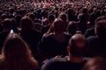 In the dark hall there is a view from the back of a crowd of hundreds of people sitting and watching the screen in a movie theater