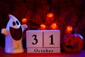 Dark halloween and fall holiday concept a calendar showing october 31 with a ghost and jack o lantern to each side and pumpkin