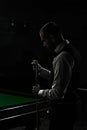 Dark image of young man in classical wear preparing cue with chalk before snooker game. Promotional poster for billiards Royalty Free Stock Photo