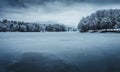 Dark landscape photo of frozen and snowy lake with forest and big hills on background - winter time. Frozen and cold lake with Royalty Free Stock Photo