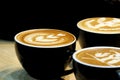 A group of hot latte coffee on a black cup with latte art on top,wooden dinning table