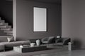 Dark living room interior with empty white framed mockup poster on wall, sofa, stairs, armchair concrete floor. Concept of Royalty Free Stock Photo