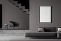 Dark living room interior with empty white framed mockup poster on wall, sofa, stairs, armchair concrete floor. Concept of Royalty Free Stock Photo