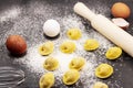 The dark marble background is covered with white flour with eggs, dumplings and a rolling pin