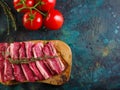 On a dark marble background, a wooden cutting board with raw pieces of meat and a sprig of fragrant rosemary, ripe tomatoes. Royalty Free Stock Photo