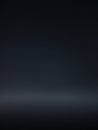A dark, minimalist studio background with a soft gradient of deep blue to black and a subtle illuminated floor line creating a Royalty Free Stock Photo