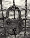 Dark monochrome close up of an old rusty padlock on a corroded metal fence against a blurred outdoor background Royalty Free Stock Photo