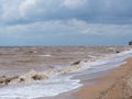 Dark muddy waves roll on the sandy shore under a stormy cloudy sky after a hurricane. Muddy sea water due to strong wind waves and Royalty Free Stock Photo