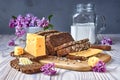 Dark multigrain bread made from rye, wheat, oats and barley with sunflower and flax seeds. Milk, cheese, butter. Lilac flowers, Royalty Free Stock Photo