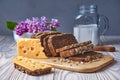 Dark multigrain bread made from rye, wheat, oats and barley with sunflower and flax seeds. Milk, cheese, lilac flowers, rustic Royalty Free Stock Photo