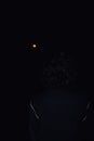 Dark night in India: Silhouette of a man mesmerized by the brilliance of a full blood moon during a total lunar eclipse