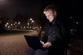 Dark night, one smiling young man, 20-29 years, sitting on bench alone, using his laptop in public park in Autumn Royalty Free Stock Photo