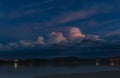 Dark ominous sky with light hitting a puff of white cloud and glowing pink