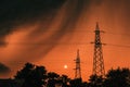 Dark ominous stormy clouds at orange summer sky, silhouettes of treetops and electricity pylon just before the rain