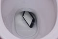 Dark phone fell in water in a toilet bowl, the top view, phone lies under water with reflection of walls of a toilet bowl