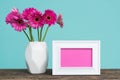 Dark pink gerberas in a vase on a table with empty picture frame greeting card. Royalty Free Stock Photo