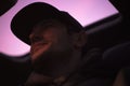 Dark portrait. Down view of young smiling hipster inside car on background of sunroof.