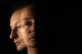 Dark portrait of a serious woman with only half her face lit up on a black background looking sad or in a depression. The face