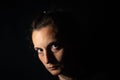 Dark profile portrait of a very dimly lit woman. The woman is looking straight ahead, conveying a feeling of mistrust or sadness