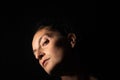 Dark profile portrait of a very dimly lit woman. The woman has her head raised and is looking straight ahead, conveying a feeling