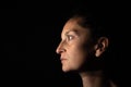 Dark profile portrait of a very dimly lit woman. The woman is looking straight ahead and transmits sadness or depression