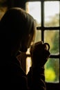 Dark profile of a woman with a cup in her hand near the window. Morning coffee