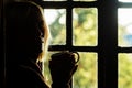 Dark profile of a woman with a cup in her hand near the window. Morning coffee