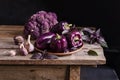 Dark purple peppers, cauliflower with leaves of basil and garlic on old rustic wooden table on black background Royalty Free Stock Photo